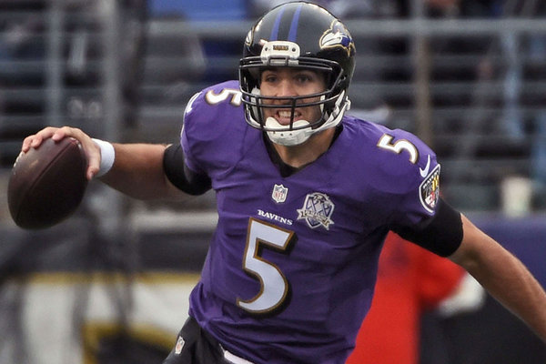 Ravens QB Joe Flacco, with the ball in his right arm, grimacing as he tries to escape pressure, wearing his purple jersey with the 20th season patch and his black pants.