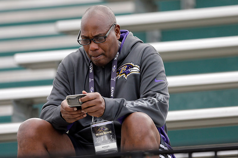 Ravens GM Ozzie Newsome sitting on the bench on his phone.