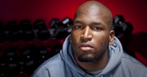 Ravens OT Eugene Monroe in front of dumbells wearing a hoodie with a serious face, thinking about marijuana advocacy.