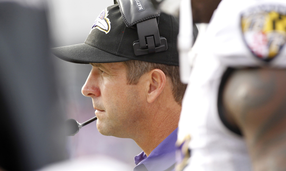 Baltimore Ravens coach John Harbaugh looks to the field in a cap and headset.