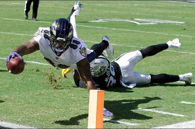 Baltimore Ravens TE Vince Mayle dives for the pylon as a Raiders defender lays on the ground behind him.
