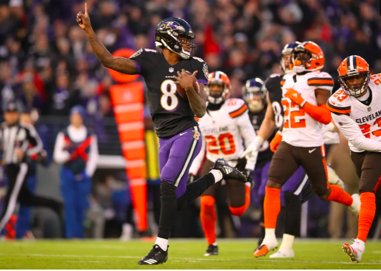 Lamar Jackson holds up a finger and runs into the end zone as Browns defenders chase.