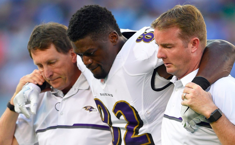 A football player is helped off the field by two trainers.