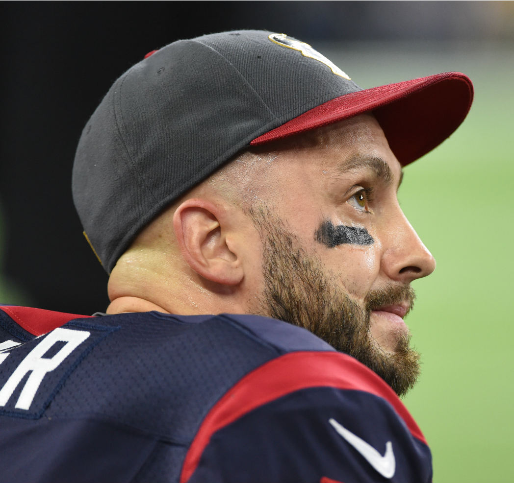 Brian Hoyer sits on the sidelines wearing his uniform with a baseball cap, looking up at the scoreboard as the Texans were clobbered by the Chiefs.